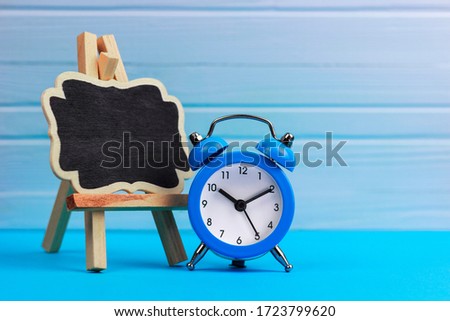 concept, time to do it , decorative easel and blue alarm clock on a blue, wooden background, place for text or advertising
