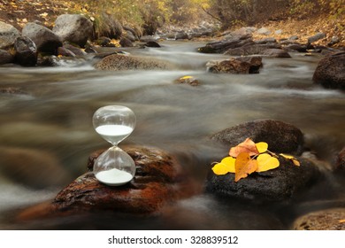 concept of time and flowing water. A hourglass on a rock of a creek.