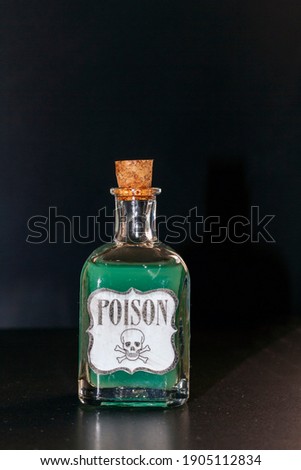 Concept of toxic thing. Transparent bottle with green liquid simulating poison. The label reads poison along with a skull and two tibias