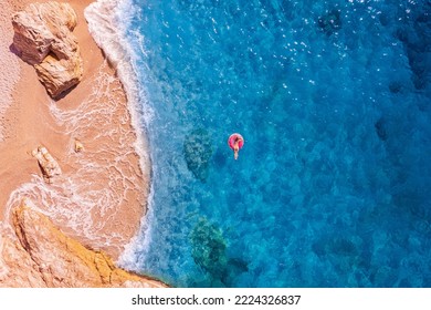 Concept travel beach resort. Young woman swimming on pink inflatable donut in turquoise sea with wave, aerial top view.