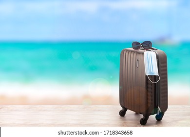 Concept Of Travel During Pandemic Time. Suitcase With Protection Mask On The Beach