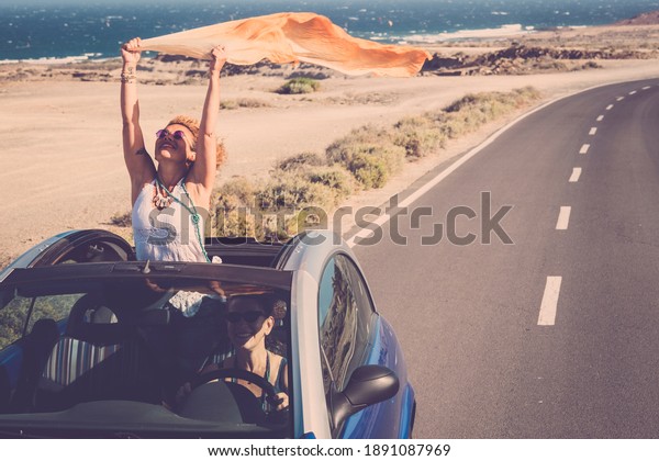 Concept of travel happiness with adult\
beautiful couple of women driving a car and enjoying the freedom\
together in friendship - people on the road with convertible\
vehicle and ocean\
background