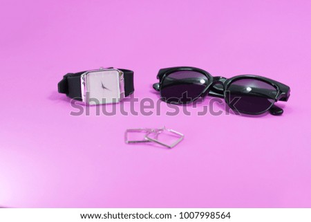 Concept travel on holiday. Sunglasses with black watch and earring on pink background.
