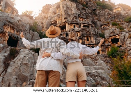 Concept travel of Turkey. Happy tourist couple man and woman in hat background old tomb Myra Ancient City in Demre to Antalya.