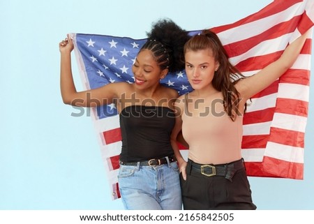 The concept of the unity of different nations and independence day of the usa - july 4. African american woman and caucasian woman holding usa flag in studio on blue background.