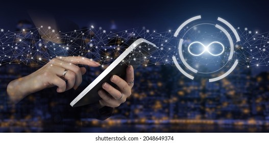 The concept of unlimited Internet. Hand touch white tablet with digital hologram infinity sign on city dark blurred background. Concept idea, life, success, business