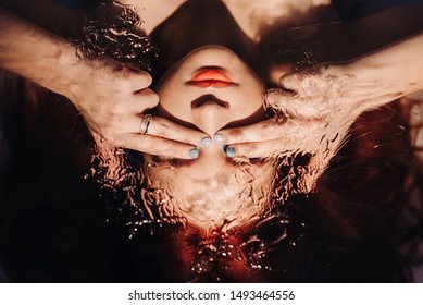 Concept of unrealistic art shooting of a mermaid under water. Surreal portrait of red haired girl like a mermaid with under water effects. through the glass close up portrait