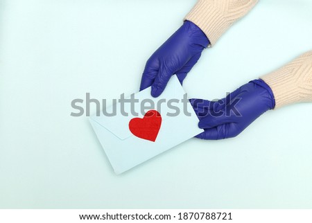The concept of Valentine's Day 2021 in the context of coronavirus. A blue envelope with a red heart in a woman's hands in blue medical latex gloves.