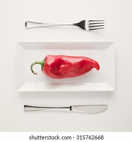 Concept Of Vegan And Vegetarian Low-carb Diet. A Single Raw And Uncut Red Pepper On A Square Rectangle Plate With Table Knife And Fork On White Background. Top Down View.