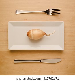 Concept Of Vegan And Vegetarian Low-carb Diet. A Single Raw Unpeeled And Uncut Onion On A Square Rectangle Plate With Table Knife And Fork. Top Down View.