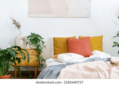 Concept Of Vintage Bedroom In Apartment With Interior Design In Style Of The 70s. Bed With Linen, Crumpled Plaid, Colorful Cushions, Cozy Bedding. Retro Side Table With Home Decor, House Plants Lush