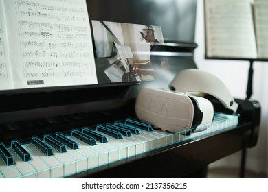 Concept Of Virtual Reality Online Class Piano Lesson From Home, VR Musical Online Learning Conceptual. Piano Teacher Instructing Student From VR Technology. AR Headset Put On Piano Keyboard. Music 3D