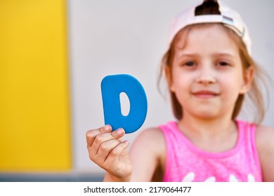 The concept of vitamin d. A little girl in a cap holds the letter D on her outstretched hand - Shutterstock ID 2179064477