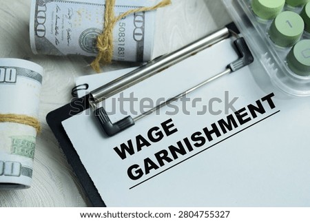 Concept of wage garnishment write on clipboard isolated on Wooden Table. For debt collection process and employee income withholding