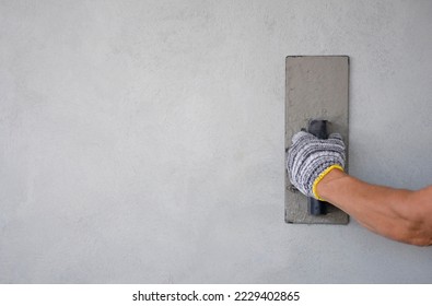 concept of wall plastering, structural work, plaster work, home building,building wall. worker hand wears glove holding trowel is plastering cement wall,concrete wall,with copy space                 