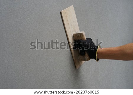 concept of wall plastering, structural work, plaster work, home building,building wall. worker hand wear glove holding wood trowel is plastering cement wall,concrete wall                       