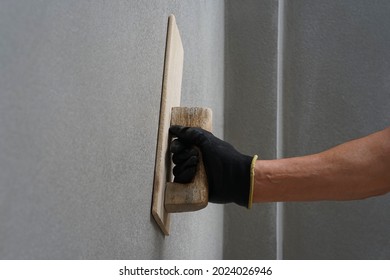 concept of wall plastering,plastering mortar,building wall surface,home building.worker wears glove holds wood spatula installing cement wall, painter hand plaster concrete house wall with trowel      - Shutterstock ID 2024026946