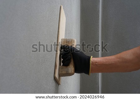 concept of wall plastering,plastering mortar,building wall surface,home building.worker wears glove holds wood spatula installing cement wall, painter hand plaster concrete house wall with trowel     