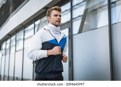 Concept of warm up and cardio exercise. Focused athlete running on the street, training outdoors. Sportsman in good shape and sportswear jacket jogging in the city at morning - Shutterstock ID 2094645997