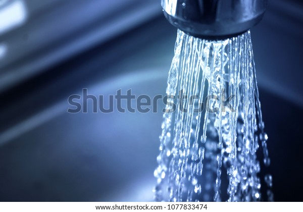 Concept water saving at home, reducing use. Water\
supply problems. Water tap with flowing water with spray. Selective\
focus