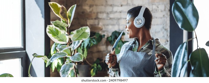 Concept of wellbeing, relaxation, work life balance, simple pleasures. Beautiful smiling plus size African American woman is doing home gardening, repotting, taking care about plants. Banner