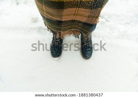 concept of winter walking in park. A man in winter boots, wrapped in plaid, stands in snow.