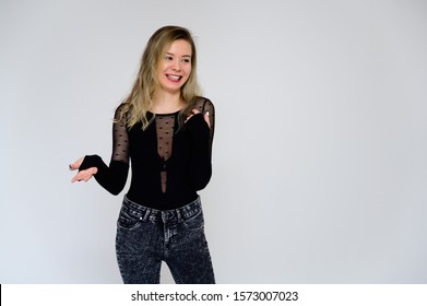 Concept Of A Woman Talking To The Camera. A Photo Of A Pretty Smiling Girl With Long Beautiful Curly Hair In A Black T-shirt On A White Background Is Standing Right In Front Of The Camera.