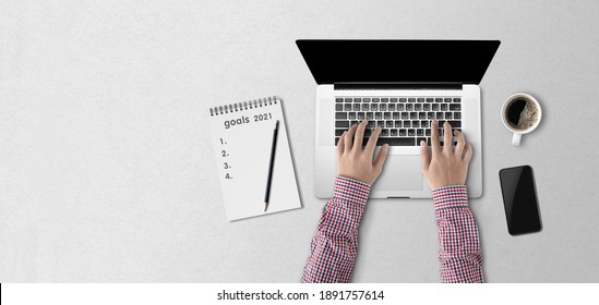 Concept Work From Home, Person Using A Laptop Computer With Blank Screen, Mug Of Coffee On The Table,mobile Phone And Write Goals 2021 In A Notebook. Top View.