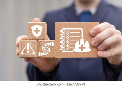 Concept Of Work Safety. Safety Officer Holding Wooden Blocks With Icon Of Checklist And Hard Hat.