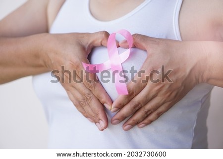 Concept : World cancer day. October Breast Cancer Awareness month. Pink ribbon on woman's chest. Hands make sign in heart shape to give encouragement for breast cancer patients                        