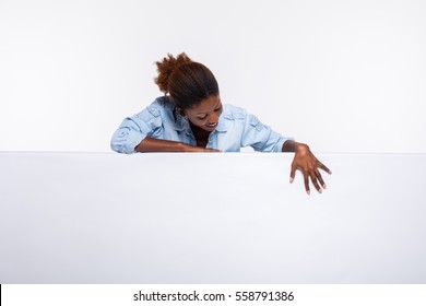 concept with young beautiful black woman leaning on an white empty and board dressed in jeans shirt and smiling presenting and pointing the subject or the text