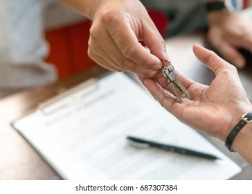 Concept young couple moving house. Hand of realtor agent giving keys of apartment to new tenant after sign rental agreement. - Shutterstock ID 687307384