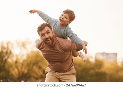 Conception of imagination, sitting on shoulders and flying. Happy father with son are having fun on the field at summertime. - Powered by Shutterstock
