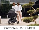 Conception of love. Young parents having a walk with baby carriage outdoors.