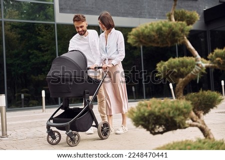 Conception of love. Young parents having a walk with baby carriage outdoors.