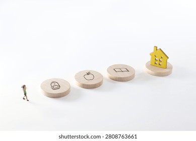 Conceptual back to school image featuring a miniature child walking toward backpack, apple, book and home icons on wooden discs. Minimal white background with ample copy space for text.