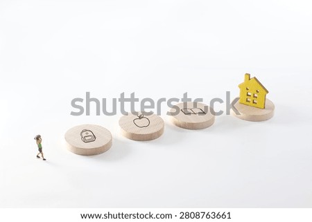 Conceptual back to school image featuring a miniature child walking toward backpack, apple, book and home icons on wooden discs. Minimal white background with ample copy space for text.
