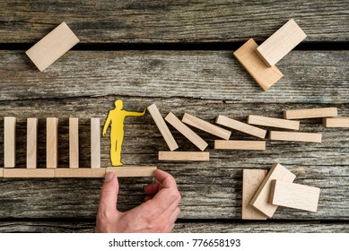 Conceptual close-up of the hand of a man offering support through a stable platform to a paper man stopping the collapse caused by domino effect.