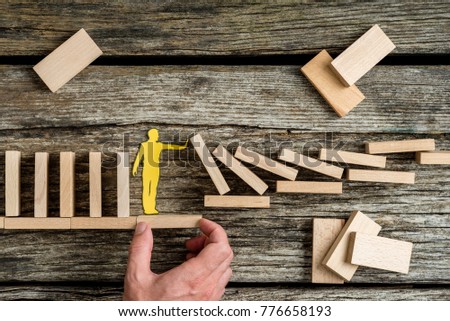 Conceptual close-up of the hand of a man offering support through a stable platform to a paper man stopping the collapse caused by domino effect.