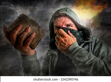 Conceptual Composite Of Radical And Violent Man . Furious Antifa And Ultra Protester With Face Mask Throwing Brick On Street Riot Chaos In Fire And Smoke In Anarchy And Revolution Concept