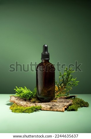 Conceptual composition of essential oils, moss and tree bark on a green background. Oil serum for skin and hair care. Glass bottles of body oil with a dropper. Self-care, Forest and nature theme.