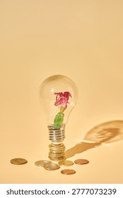 Conceptual composition: financial crisis. Withered flower in a light bulb on a stack of coins on beige background. Metaphor for failed innovation, unprofitable startup, and economic loss.