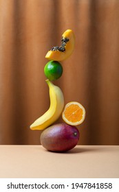 Conceptual creative still life with balancing fruits, such as mango,orange and papaya over fabric background, vertical