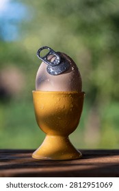Conceptual egg with aluminum pull tab in holder outdoor, close up. Creative concept of fresh egg with an easy open metal can tab in yellow ceramic cup on wooden table