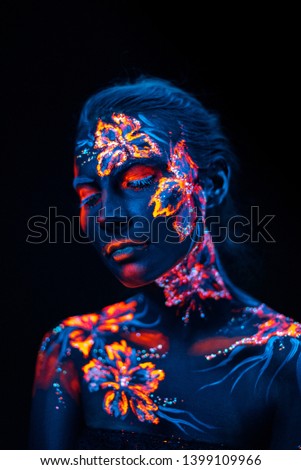 Conceptual face art with shining flowers painted in fluorescent colors isolated on black background