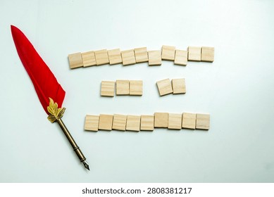 A conceptual flat lay featuring a red feather quill pen next to blank wooden tile blocks arranged in lines on a clean white background, symbolizing writing and censorship