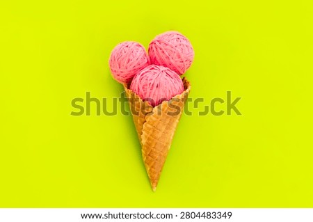 Conceptual flat lay of three pink yarn clew balls arranged like scoops of ice cream inside a waffle cone on a vibrant neon green surface.