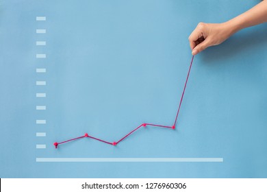 Conceptual hand pulling business finance growth chart line upwards on blue background. 