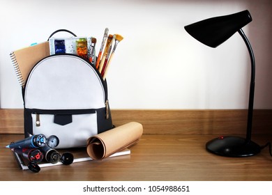 
Conceptual image of Artist graphic designer backpack. Backpack, notebook, album, folded paper, paint, tube ink, watercolor, brushes on a wooden table. Back to school and happy time! 
