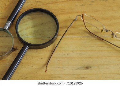 Conceptual Image Of Business Surveillance Scrutiny Oversight. Top View Of 2 Magnifying Glasses And Eyeglasses On Wooden Surface. Selective Focus.